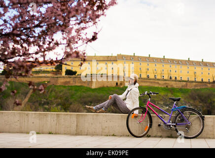 Jolie jeune femme en profitant de la vue après le tour de vélo avec le vélo à côté.Elle est assise sur le mur et à la rive du Danube vers Banque D'Images