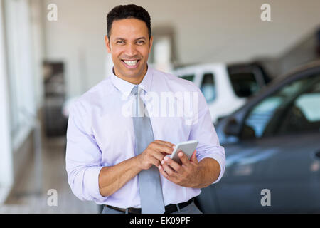 Bel homme d'âge moyen à l'aide de smart phone at car dealership Banque D'Images