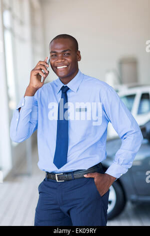 Heureux salesman talking on mobile phone in vehicle showroom Banque D'Images