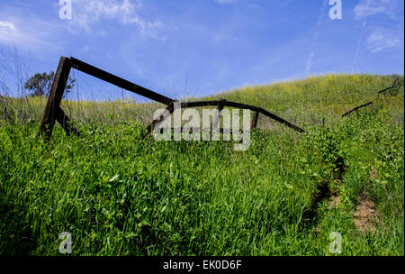 Vieille clôture, ventilés sur une colline herbeuse contre un ciel bleu. La clôture monte et sur les collines. Banque D'Images