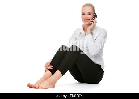 Blonde smiling businesswoman assis sur le plancher et à l'aide de mobile phone Banque D'Images