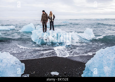 Vue sur l'océan avec deux personnes sur le haut d'un iceberg près de la lagune glaciaire du Jökulsárlón dans le sud de l'Islande Banque D'Images