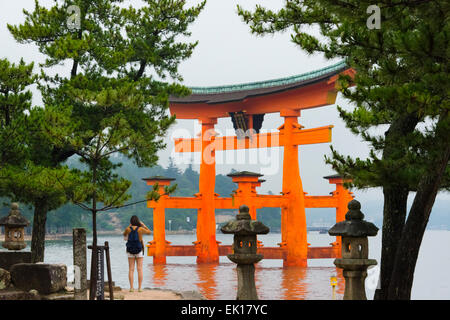 Girl photographing Torii du sanctuaire d'Itsukushima, Miyajima, Japon Banque D'Images