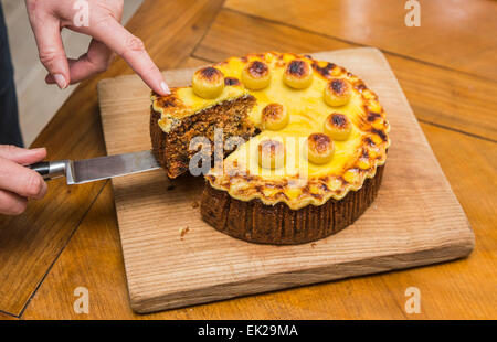 Tranche en cours de suppression sur un couteau de cuisine et servi d'une maison traditionnelle fraîchement coupé Easter simnel cake sur une planche à découper en bois Banque D'Images