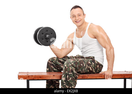 Beau jeune bodybuilder l'entraînement avec un barbell métallique assis sur un banc en bois isolé sur fond blanc Banque D'Images