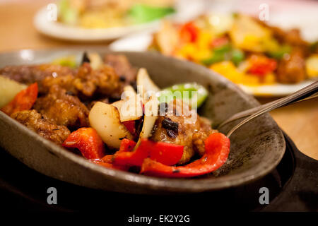 La cuisine chinoise : faire revenir le poulet et les légumes dans une sauce aux haricots noirs, servis sur une plaque en fonte, à chaud. Banque D'Images