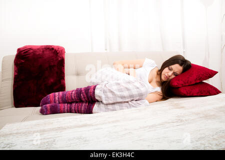 Jeune femme au canapé avec douleur période Banque D'Images