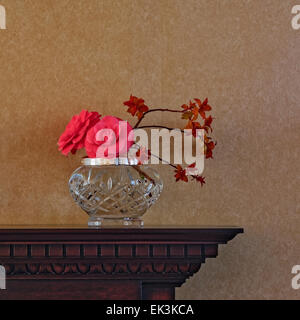 Arrangement de fleurs, y compris les fleurs de camélia, dans un ​Crystal vase sur la cheminée en bois sculpté ; fond d'ordinaire contre format carré. Banque D'Images