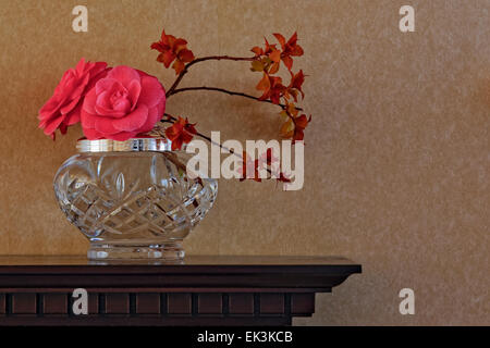 Arrangement de fleurs, y compris les fleurs de camélia, dans un ​Crystal vase sur la cheminée en bois sculpté ; fond d'ordinaire contre l'orientation paysage. Banque D'Images