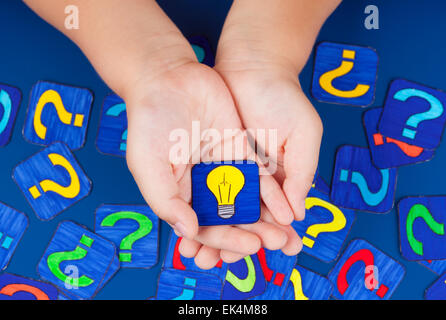 Ampoule jaune dans les mains de l'enfant sur fond bleu avec beaucoup de points d'interrogation. Photos dessiné par moi. Banque D'Images