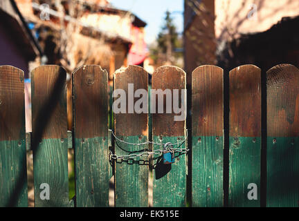 Vieille porte en bois verrouillée avec une chaîne et un cadenas. Jardin floue et maisons dans l'arrière-cour. Banque D'Images