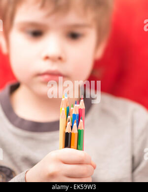 Little girl holding colorful crayons à la main. Il est à les regarder avec un visage sérieux. Banque D'Images