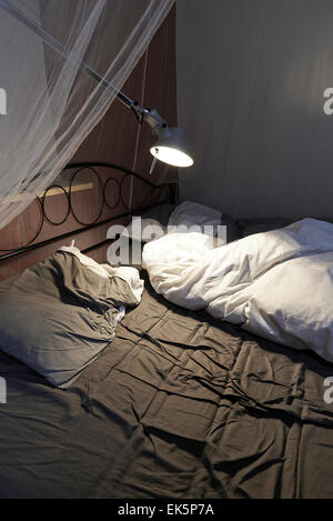 Draps et oreillers échevelée d'un lit défait, led lumière et moustiquaire Banque D'Images