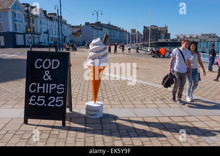 Aberystwyth, Pays de Galles, Royaume-Uni. 7 avril, 2015. Météo France : Les gens se promener au soleil sur la promenade de Aberystwyth publicité signes passés des glaces et des fish and chips Crédit : Alan Hale/Alamy Live News Banque D'Images