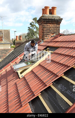 Un constructeur de l'installation d'un velux sur un toit aigu dans le sud de Londres Banque D'Images