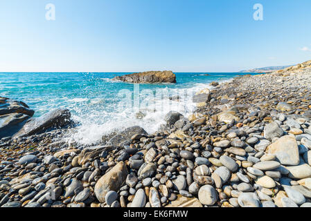 Les graviers de vagues se brisant sur l'eau, les cailloux et les rochers d'une plage vide dans la rude côte rocheuse de la Ligurie, au nord de l'Italie. Banque D'Images