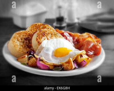 Le petit déjeuner anglais complet avec des crumpets, servi sur une plaque blanche dans une table - œuf frit, bacon, pommes sautées et les crumpets Banque D'Images