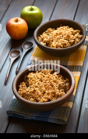 Deux bols rustiques de Crumble pomme au four ou sur une serviette de cuisine, cuillères en bois et des pommes fraîches sur le côté Banque D'Images