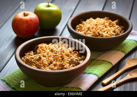 Deux bols rustiques de Crumble pomme au four ou sur une serviette de cuisine, cuillères en bois et des pommes fraîches sur le côté Banque D'Images