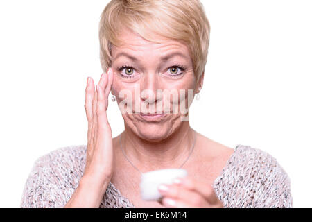 Middle-aged attractive blonde woman applying crème anti-vieillissement pour les rides autour de ses yeux dans un effort pour lutter contre le vieillissement Banque D'Images