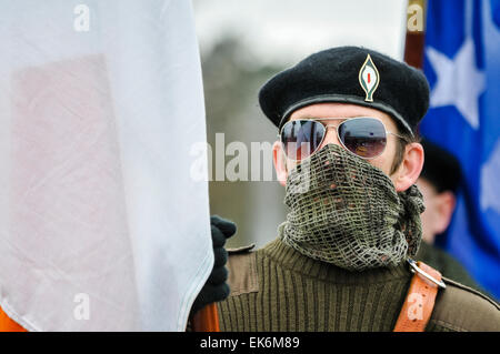 Un homme masqué portant un scrim sur sa bouche, lunettes de soleil et un béret noir est titulaire d'un drapeau au cours d'une commémoration Républicaine Irlandaise Banque D'Images