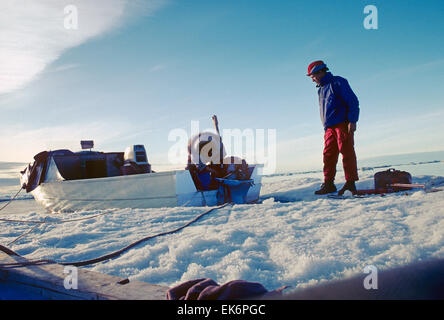 Chasseur inuit autochtones réparation moteur hors bord sur son canot de fret des Inuits. Photographe américain Mark H. Weidman regarde sur. Banque D'Images
