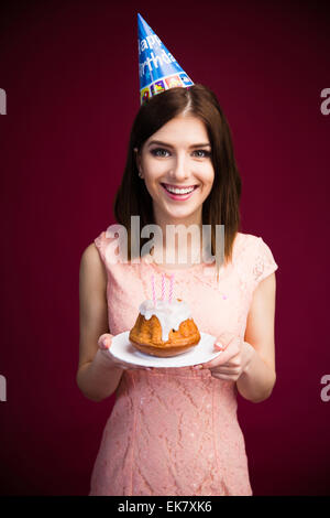 Smiling Pretty woman holding cake avec des bougies sur fond rose. En regardant la caméra. Célébrant son anniversaire ! Le port de la broche Banque D'Images