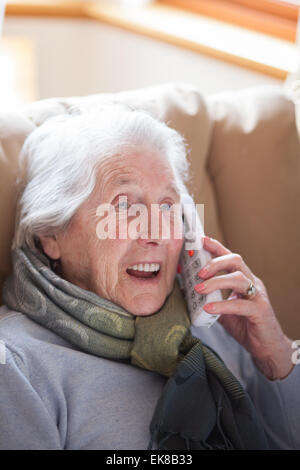 Vieille dame assise dans un fauteuil à parler au téléphone Banque D'Images