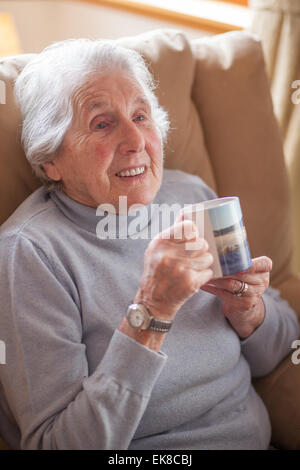 Vieille dame se détend dans un fauteuil avec une tasse de thé Banque D'Images