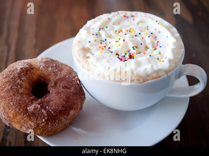 Un gâteau chaud avec sprinkles couleur latté et crème fouettée, le sucre et d'un beignet à la cannelle. Banque D'Images