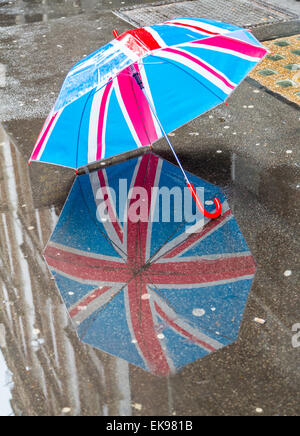 Une Union Jack réflexion parapluie dans une flaque d'eau de pluie dans une rue de Londres, London England UK Banque D'Images