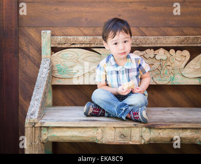 Décontracté Cute Boy assis sur un banc en train de manger son sandwich. Banque D'Images