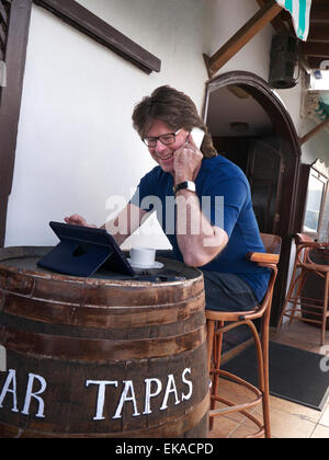 L'homme à l'aide de son iPhone 6 et iPad mini tablet computer à l'étranger à l'alfresco restaurant bar à tapas espagnol Banque D'Images