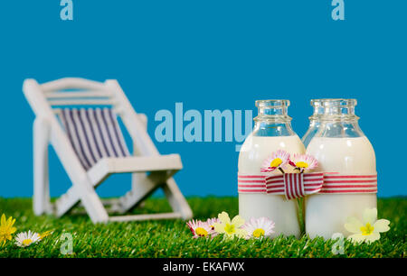 Trois petites bouteilles de lait avec une chaise de salon dans l'herbe Banque D'Images