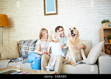 Jolie petite fille et ses parents avec chien reposant sur canapé à la maison Banque D'Images