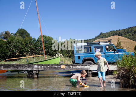 Garçons jouant avec télécommande toy boat on Lake Okareka, Nouvelle-Zélande Banque D'Images