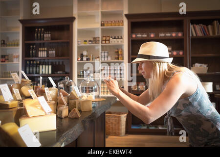 Young woman photographing fromages sur smartphone dans l'épicerie bio Banque D'Images