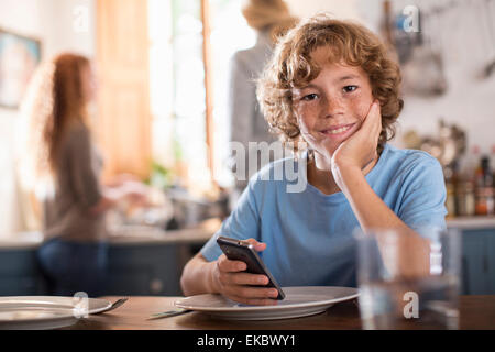 Teenage boy holding smartphone à table à manger Banque D'Images