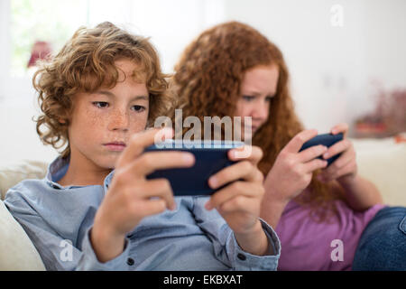 Frères et sœurs jouant avec l'ordinateur de poche sur le plateau de jeu Banque D'Images