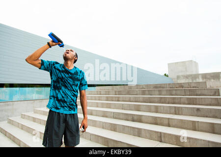 Young male runner l'eau potable sur les étapes de la ville Banque D'Images