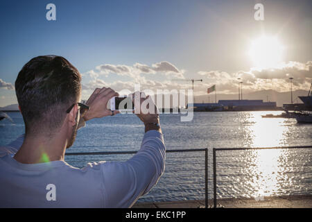 Jeune homme de prendre photo de coucher de soleil par port, Cagliari, Sardaigne, Italie Banque D'Images