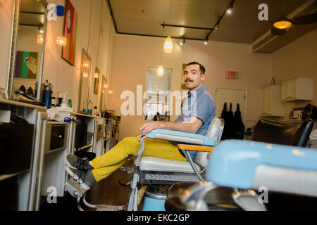 Jeune homme assis sur une chaise dans un salon de coiffure Banque D'Images
