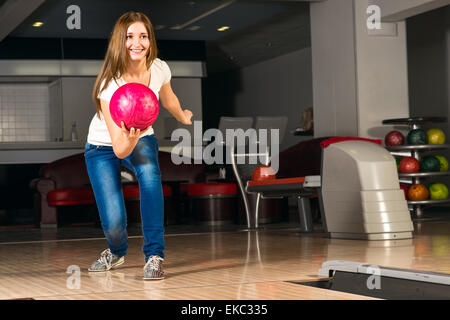 Agréable jeune femme jette une boule de bowling Banque D'Images