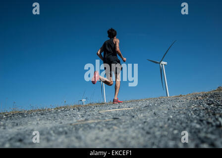 Mid adult man jogging jusqu'à une colline vers les éoliennes Banque D'Images