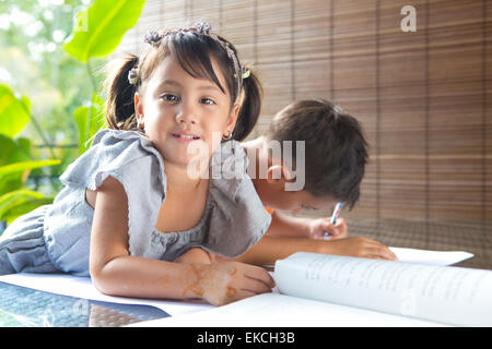 CuteÊlittle pan asian girl smiling with a story book assis à côté d'un grand frère absorbé par activité de coloriage dans home env Banque D'Images