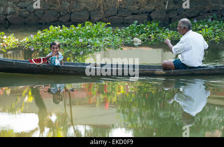 Un homme et jeune garçon dans un canot sur les eaux troubles de Kumarakom, Kerala Inde Banque D'Images