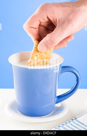 La main de l'homme un biscuit trempé dans une tasse de lait bleu Banque D'Images