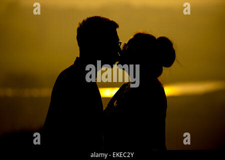 Un couple embrasser et partager un baiser au coucher du soleil sur un ciel voilé summers day en Angleterre, Royaume-Uni. Banque D'Images