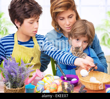 Famille heureuse peinture oeufs de Pâques à la maison mère, avec deux adorables fils et chat mignon faire alimentaire décoratif traditionnel de Pâques Banque D'Images