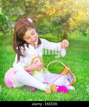 Cute little girl playing jeu traditionnel de Pâques, chasse aux oeufs colorés, s'amuser dans le jardin vert frais avec mignon bunny Banque D'Images